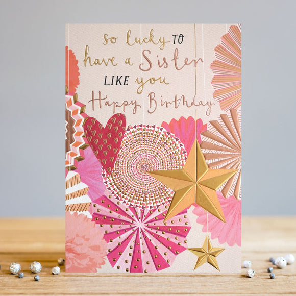 The perfect birthday card to show your sister how much you love her! This birthday card is decorated in a contemporary style, with a display of pink and gold star, pom-pom and heart hanging party decorations. Metallic text on the front of the card reads 