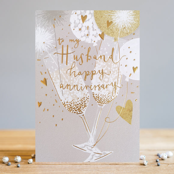 This anniversary card for a special husband is perfect for celebrating any wedding anniversary. Decorated with an elegant grey, white and gold design of two champagne flutes clinking together amid a burst of balloons, golden confetti and sparklers, gold text on the front of the card reads 
