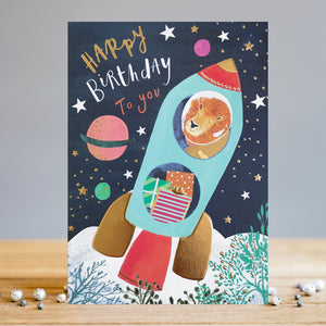 Say happy birthday with a card that's truly out of this world! This Louise Tiler birthday card is decorated with an illustration of a lion blasting off into outer space in a rocket loaded with presents, flying through a sky filled with brightly coloured stars and planets. The text on the front of the card reads "Happy Birthday to you".