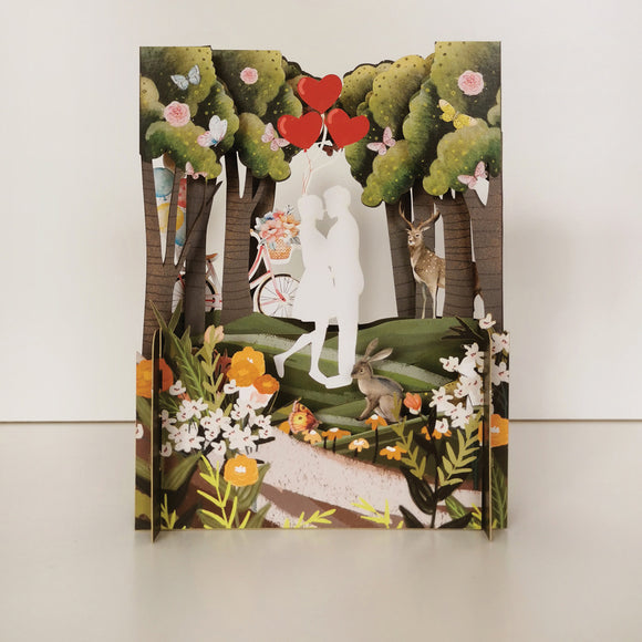 Perfect for weddings or valentines day, this fabulous pop-up greetings card is made of multiple layers of laser cut card to create a wonderful 3d image showing a scene of a couple kissing in a lush forest.