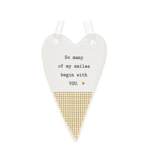This ceramic plaque from Thoughtful Words Ceramics is an ideal gift to remind a romantic partner or a cherished family member know you're thinking of them. The white glazed heart is decorated with black text that reads "So many of my smiles begin with you", above a gold mesh design.