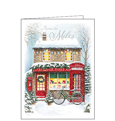 This christmas card is perfect for sending festive wishes across the miles. This card is decorated with an illustration by Rob Parkinson showing a snow-covered village post office with a festive decoupage of a red telephone box and bicycle. The caption on the front of the card reads 