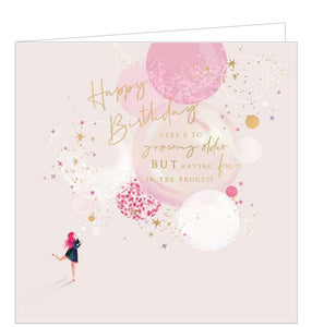 This beautiful birthday card features a sketch of a young woman with bright pink hair blowing bubbles, with large bubbles floating off in the background against a pink backdrop. Gold text on the front of the card reads "Happy Birthday...Here's to growing older but having fun in the process".