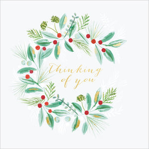 This lovely Christmas card for is decorated with a wreath of green foliage and red berries surrounding gold text that reads "thinking of you".