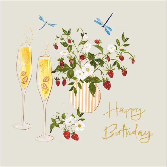 This birthday card features a sketch of a strawberry plant in a pot and two glasses of champagne. Two blue dragonflies are over head and simple gold text reads 