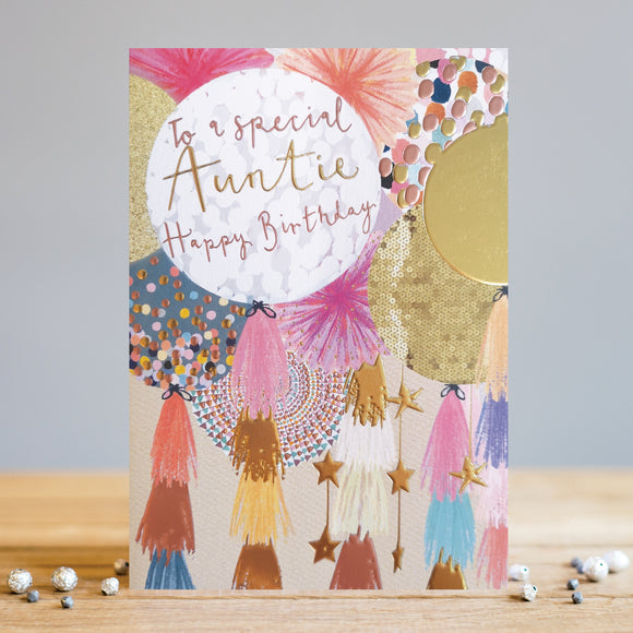 This birthday card for a special aunty features a modern and eye-catching design with gold detailing. This birthday card is decorated with a close-up illustration of colourful balloons in shades of pink, peach and gold. Each balloon has tassels and stars hanging from their strings.The text on the closest balloon reads 