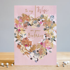 Express your love to your wife with this exquisite Louise Tiler birthday card. Featuring a charming heart-shaped floral wreath, gilded gold finishes, and a delicate pink background, this card will make her special day one to remember. Rose gold text reads "To my Wife on your Birthday".
