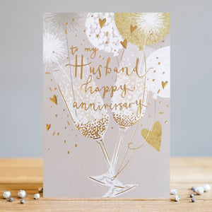 This anniversary card for a special husband is perfect for celebrating any wedding anniversary. Decorated with an elegant grey, white and gold design of two champagne flutes clinking together amid a burst of balloons, golden confetti and sparklers, gold text on the front of the card reads "To my Husband...Happy Anniversary".