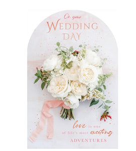 This elegant wedding day card is decorated with the photographic image of a white bouquet with pink ribbon, surrounded by rose gold mini hearts. The top edge is arched.  The pink and gold script on the front of the card reads "On your Wedding day...love is one of life's most exciting adventures".