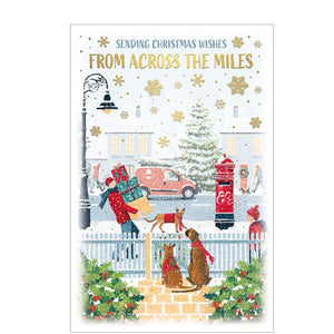 Perfect for sending to friends, family or loved ones far away, this Christmas card is decorated with a scene of a pair of dogs, dressed for the snow in knitted scarves, fitting just inside their garden fence watching people on the street busy with festive tasks.

The caption on the front of this Christmas card reads "Sending Christmas wishes From Across the Miles".