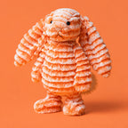Official Jellycat (jelly cat) independent shop release of a cute and cuddly orange bunny called Fizzleskip for the autumn and winter 2026 season. Image shows a standing Fizzleskip on an orange abckground