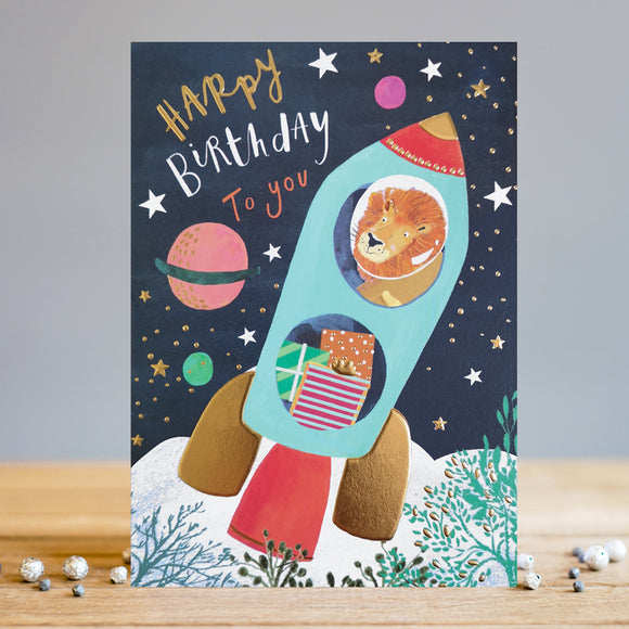 Say happy birthday with a card that's truly out of this world! This Louise Tiler birthday card is decorated with an illustration of a lion blasting off into outer space in a rocket loaded with presents, flying through a sky filled with brightly coloured stars and planets. The text on the front of the card reads 