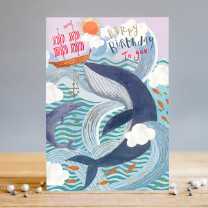 This stunning Louise Tiler birthday card is decorated with a majestic scene of adventure and daring as a tiny ship sails bravely through huge waves, watched by gigantic blue whales and schools of goldfish. The caption on the front of the card reads "Happy Birthday to you".  This beautiful design, finished with tiny gold detailing, captures the majesty of the sea and makes for a wonderful card to add a unique touch to any Birthday celebration. 
