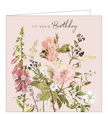 This is a stunning birthday card decorated with an illustration of a bumble gathering nectar from dreamy pink and gold flowers. Gold text in the top corner of the card reads 