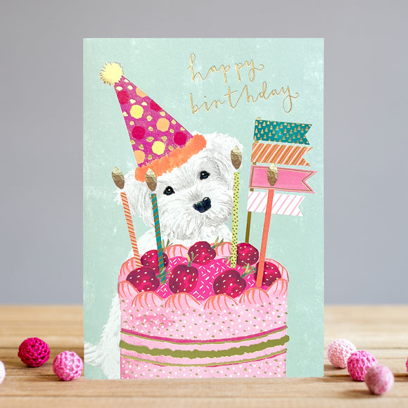 This adorable birthday card from artist Louise Tiler is decorated with a white westie dog, wearing a party hat, looking wistfully at a large pink birthday cake topped with candles and flags. Gold text on the front of the card reads 