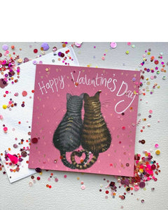 The lovely Valentine's card features Alex Clark's illustration of two cats sitting close together, their tails entwined to create a heart, surrounded by a raspberry coloured, heart dotted background. White text above the cats reads "Happy Valentine's Day".