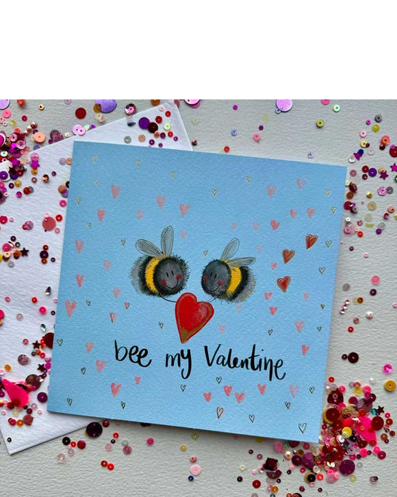 A wonderfully cute Valentine's card by Alex Clark, featuring two romantic bees holding red heart between them. The background is blue and dotted with mini heart details. Black script on the front of the card reads 