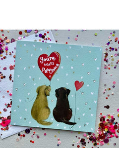 The lovely Valentine's card features Alex Clark's illustration of two dogs sitting close, surrounded by a sage coloured, heart dotted background. One dog holds a red heart-shaped balloon which reads "You're totally Pawsome", the other dog has a smaller heart-shaped balloon tied to its tail.