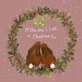 Part of Alex Clark's Christmas card collection, this Christmas card is decorated with a festive wreath, inside of which two rabbits snuggle together under the mistletoe. White text on the front of the card reads "to the One I Love at Christmas x".