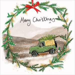 Part of Alex Clark's Christmas card collection, this Christmas card is decorated with Alex's painting of a black labrador dog seemingly driving a landrover -with christmas tree on the roof- over a snowy moor. A Christmas wreath forms a border. The text on the front of the card reads "Merry Christmas".