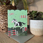Sweet and small, alex Clark Blank Card showing a Piebald Horse among Jumps in a green field. the top of the card has a scalloped edge
