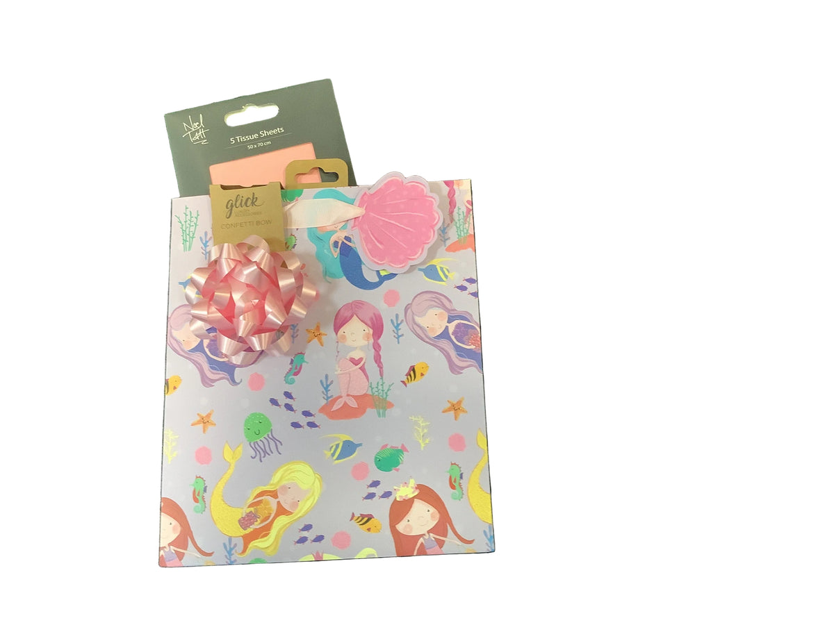 A gift bag with a mermaid-themed pattern on a light gray background, decorated with a pink and white bow and a pink seashell gift tag with salmon pink tissue paper