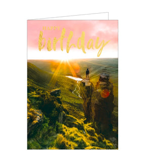 This birthday card is decorated with a photograph of a person standing alone on top of a rocky outcrop as dawn breaks.. Gold text on the card reads "Happy Birthday".