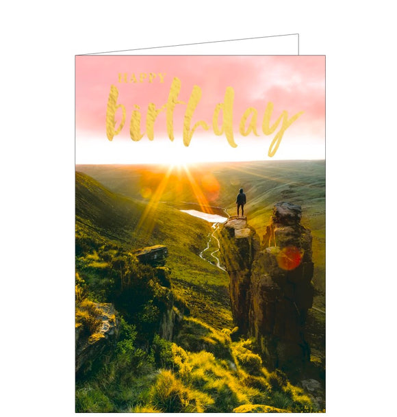 This birthday card is decorated with a photograph of a person standing alone on top of a rocky outcrop as dawn breaks.. Gold text on the card reads 