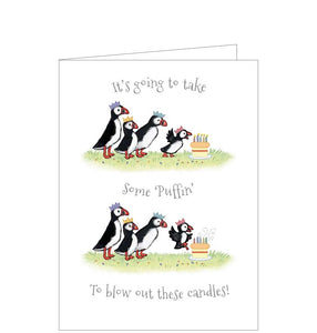 This adorable birthday card is decorated a family of puffin birds throwing a birthday party with a little puffin blowing out candles on a birthday cake. Silver text on the front of the card reads "It's going to take some 'PUFFIN' to blow out these candles!"