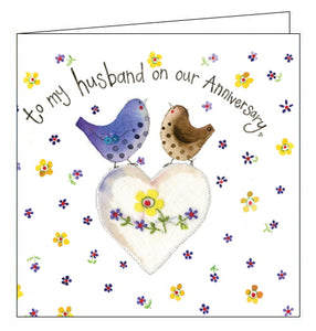 Part of Alex Clark's "Sparkle" card Collection, finished with a dusting of glitter. This anniversary card for a special husband is decorated with two birds standing on a heart. The text on the front of the card reads "to my husband on our anniversary".