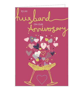 This anniversary card for a special husband is decorated with two gold metallic champagne coupes clinking together and overflowing with metallic and glittery hearts. The text on the front of the card reads "To my husband on our Anniversary".
