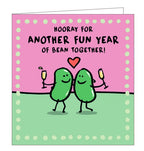 This anniversary card is decorated with a pair of cartoon beans, with their arms around each other, raising glasses of champagne. The text on the front of the card reads "Hooray for another fun year of bean together!"