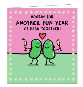 This anniversary card is decorated with a pair of cartoon beans, with their arms around each other, raising glasses of champagne. The text on the front of the card reads "Hooray for another fun year of bean together!"