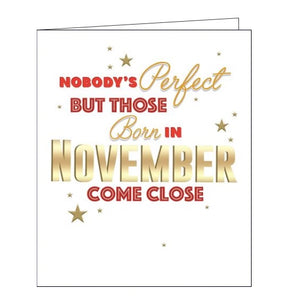 This birthday card is decorated with red, and gold script that reads "Nobody's perfect but those born in November come close". Embossed gold stars are sprinkled around the text.