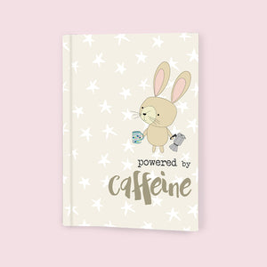 This softbacked A6 lined notebook is decorated with a cute bunny rabbit holding a moka pot in one paw and a cup of coffee in the other. The caption on the front of the note book reads "Powered by caffeine.". 