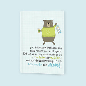 This softbacked A6 lined notebook is decorated with a brown bear in a woolly jumper holding a coffee cup in one hand and a bottle of gin in the other. The caption on the front of the note book reads "you have now reached the age where you will spend 50% of your day wondering if it's too late for coffee...and 50% deliberating if it's to early for alcohol...". 