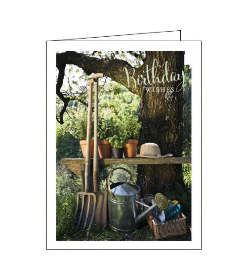 This birthday card is decorated with a photograph of a garden bench, beside a tree, laiden with potted plants and garden tools. The text on the front of the card reads 