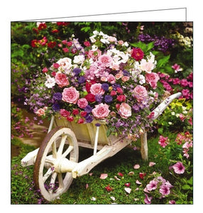 This blank card is decorated with a photograph of a wooden wheelbarrow planted with pink, purple and white flowers.