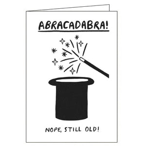 This funny birthday card is decorated with a black and white drawing of a magic wand being waved over a top hat. The caption on the front of the card reads "ABRACADABRA! Nope, still old!"