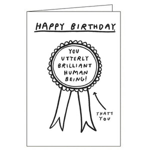 This cute birthday card is decorated with a black and white drawing of a rosette that reads "You utterly brilliant human being!" The caption on the front of the card reads "Happy Birthday"