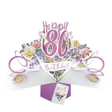 A spectacular pop-up 3D keepsake 80th birthday card, that opens to unleash pink streamers, delicate flowers and text that reads "Happy 80th Birthday".