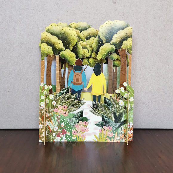 This fabulous pop-up greetings card is made of multiple layers of laser cut card to create a wonderful 3d image showing a scene of a couple, holding hands as they walk through a lush forest.